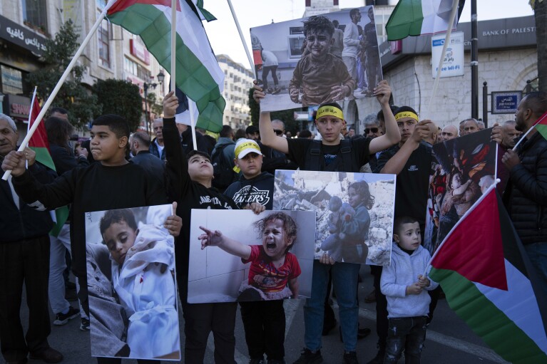 Demonstrators carry posters with pictures of Palestinians killed during the current conflict in Gaza and fly Palestinian flags during a rally in solidarity with Gaza, in the West Bank city of Ramallah, Monday, Dec. 11, 2023. (AP Photo/Nasser Nasser)