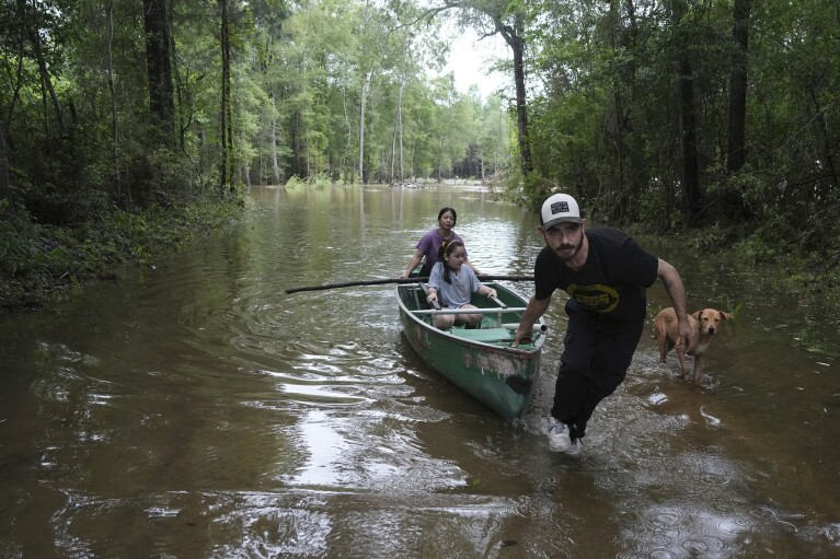 ARQUIVO - Alvaro Trevino reboca uma canoa com Jennifer Tellez e Aileen, após visitarem sua casa no dia 5 de maio de 2024, em Spindora, Texas.  Num mundo que se tornou cada vez mais habituado a condições climáticas extremas, os últimos dias e semanas parecem ter levado os extremos ambientais a um novo nível.  (Elizabeth Conley/Houston Chronicle via AP, Arquivo)
