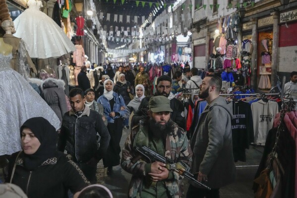 An armed opposition fighter walks among costumers at the Al-Hamidiyeh market inside the old walled city of Damascus, Syria, Tuesday, Dec. 10, 2024. (AP Photo/Hussein Malla, File)