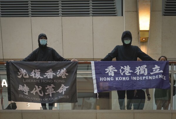 FILE - In this June 9, 2020, file photo, protesters show a banner "Librate Hong Kong, Revolution of out time," left, and "Hong Kong Independence" in a shopping mall during a protest in Hong Kong. The slogans had just been banned by the government under the new legislation, stating that it had separatist connotations. (AP Photo/Vincent Yu, File)