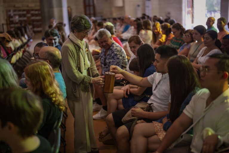 A volunteer holds a box while taking donations from the faithful during a Mass in the Sagrada Familia basilica in Barcelona, Spain, Sunday, July 9, 2023.  (AP Photo/Emilio Morenatti)