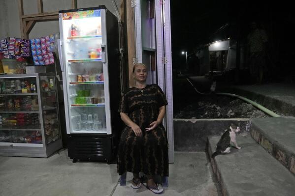 Jarmilah poses for a photo at her convenience store on Karampuang Island whose electricity relies on solar power plants, in West Sulawesi, Indonesia, Thursday, Dec. 22, 2022. While Indonesia has vast renewable and green energy potential from solar, wind, geothermal and other sources, experts warn that the vast archipelago nation faces unique financial, policy, infrastructure and other challenges that will require innovation.(AP Photo/Dita Alangkara)