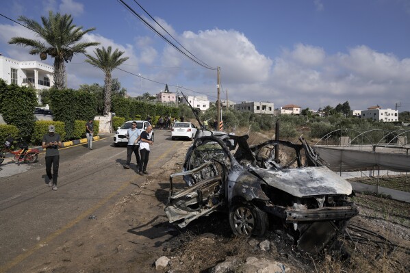 Palestinians gather around a car destroyed in a drone strike Zeita village, north of the West Bank city of Tulkarem, Saturday, Aug. 3, 2024. The Israeli military says it struck five suspected terrorists in a vehicle on their way to carry out an attack. (AP Photo/Majdi Mohammed)