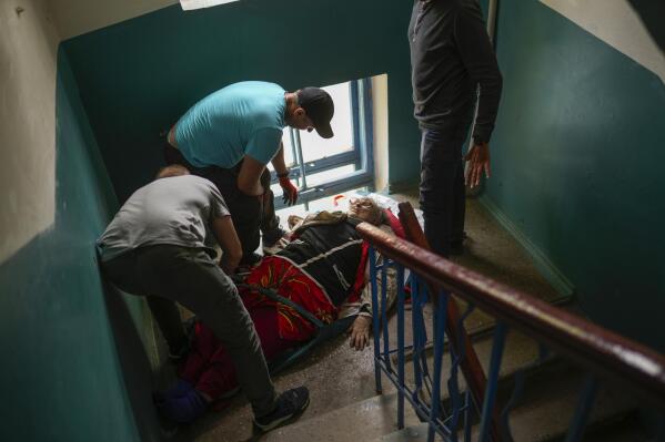 A woman is carried down a staircase from her home during an evacuation by volunteers from the Vostok SOS charitable organization in Kramatorsk, eastern Ukraine, Thursday, May 26, 2022. (AP Photo/Francisco Seco)