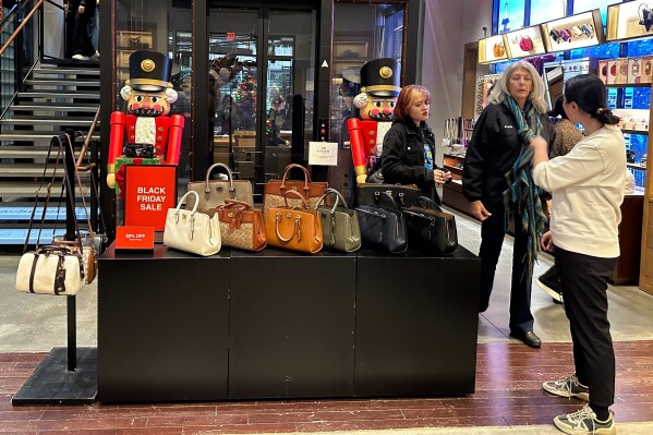 Shoppers pause near a display of handbags at a Coach store in New York on Sunday, Nov. 19, 2023. Retailers are kicking off the unofficial start of the holiday shopping season on Friday with a bevy of discounts and other enticements. (AP Photo/Anne D'Innocenzio)
