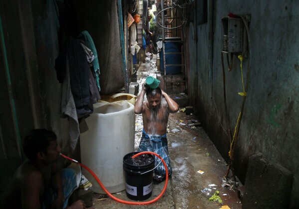 FILE - In this Thursday, July 10, 2014, file photo, a man bathes outside his house in Dharavi, one of Asia's largest slums, in Mumbai, India. Set between busy train tracks and the heavily polluted Mithi River, which separates the slum from Mumbai’s modern skyscrapers, the neighborhood is a maze of tiny alleys, each one full of scores of people who live in tin shacks. Families or groups of migrant workers often pile into a single room. Hardly anyone has a private bathroom. (AP Photo/Rafiq Maqbool, File)