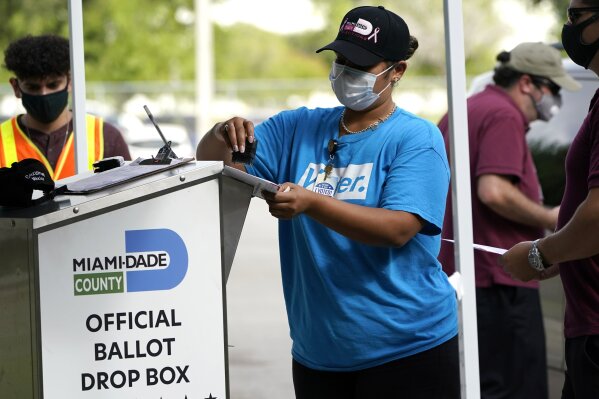 FILE - In this Monday, Oct. 26, 2020, file photo, an election worker stamps a vote-by-mail ballot dropped off by a voter before placing it in an official ballot drop box before at the Miami-Dade Co...