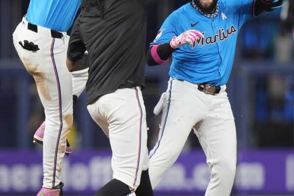 Miami Marlins' Bryan De La Cruz (14) and Edward Cabrera, center, celebrate with Emmanuel Rivera, right, after Rivera hit a single scoring Nick Fortes to beat the Philadelphia Phillies 7-6 in the 10th inning of a baseball game, Sunday, May 12, 2024, in Miami. (AP Photo/Wilfredo Lee)