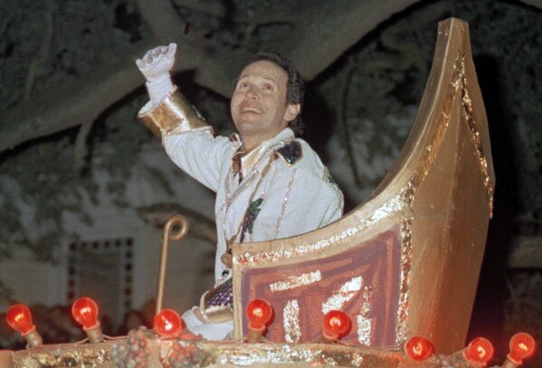 Comedian Billy Crystal tosses doubloons from a float in the Bacchus parade in New Orleans, Feb. 6, 1989, during Mardi Gras celebrations. Thousands turned out to see Crystal as Bacchus, the God of Wine and Revelry despite slight mist and cold temperatures. (AP Photo/Mary Foster, file)