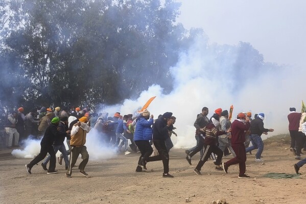 Farmers run for cover after police fired tear gas to disperse protesting farmers who were marching to New Delhi near the Punjab-Haryana border at Shambhu, India, Tuesday, Feb.13, 2024. Farmers are marching to the Indian capital asking for a guaranteed minimum support price for all farm produce. (AP Photo/Rajesh Sachar)