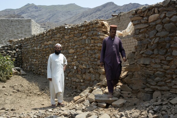 Local residents stand beside a wall damaged due to cross firing between Pakistan and Afghan Taliban forces near Torkham border area of Nangarhar, province east of Kabul, Afghanistan, Tuesday, Aug. 13, 2024. Pakistani and Afghan Taliban forces traded cross-border fire near a key northwestern crossing, killing a woman and two children on the Afghan side of the border, officials said Tuesday. (AP Photo/Shafiullah Kakar)