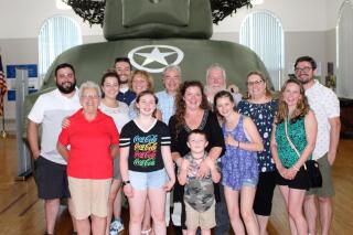 This photo provided by Andrea J. Cheeney shows four generations of the McKane family pose with an inflatable tank at the Ghost Army exhibit on June 7, 2021 at Historical Society of Cheshire County, Keene N.H. Their patriarch and local resident Mickey McKane was involved with the Ghost Army Unit. Members of two top-secret World War II military units referred to as the “Ghost Army” will be awarded the Congressional Gold Medal more than 75 years after their service, under legislation signed into law by President Joe Biden, Tuesday, Feb. 1, 2022. ( Andrea J. Cheeney via AP)