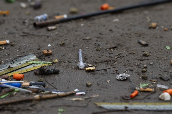 A used needle is seen next to orange syringe caps on the ground on Friday, March 22, 2024, in Baker Park in Grants Pass, Ore. (AP Photo/Jenny Kane)