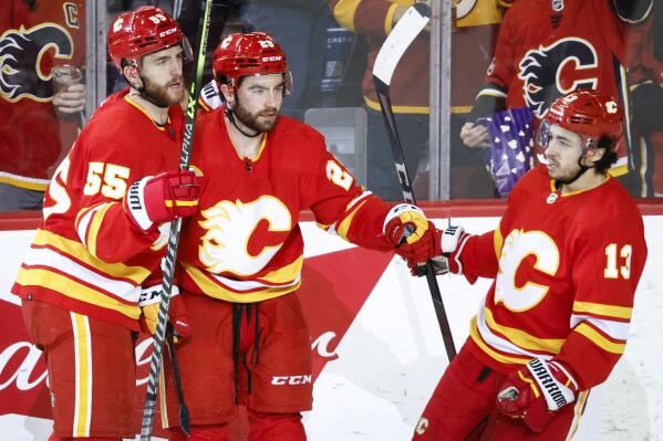 Calgary Flames' Dillon Dube, center, celebrates his goal with against the New Jersey Devils with Noah Hanifin, left, and Johnny Gaudreau during the second period of an NHL hockey game Wednesday, March 16, 2022, in Calgary, Alberta. (Jeff McIntosh/The Canadian Press via AP)