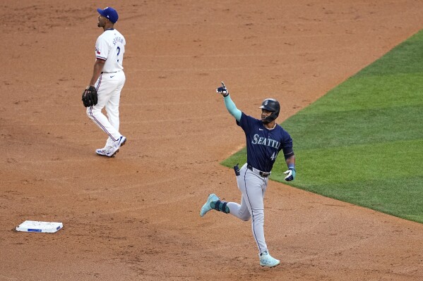 Seattle Mariners' Julio Rodriguez celebrates his two-run home run as he jogs past Texas Rangers second baseman Marcus Semien during the third inning of a baseball game in Arlington, Texas, Tuesday, April 23, 2024. (AP Photo/Tony Gutierrez)