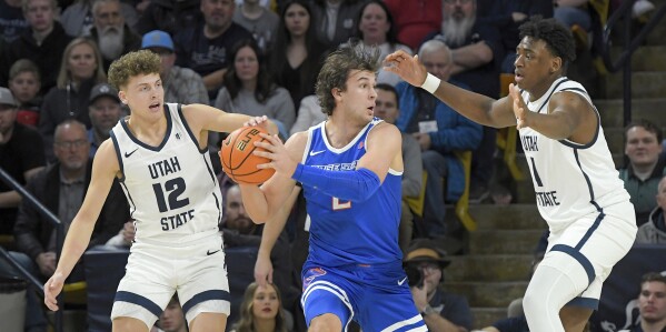 El delantero de Boise State, Tyson Degenhart, busca pasar el balón mientras el guardia de Utah State, Mason Falslev (12) y el delantero Great Osobor (1) defienden durante la primera mitad de un partido de baloncesto universitario de la NCAA el sábado 10 de febrero de 2024 en Logan, Utah.  (Eli Lucero/The Herald Journal vía AP)