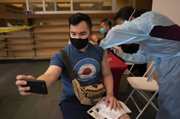 FILE - In this April 12, 2021, file photo, Freeson Wong, 31, takes a selfie as he receives a dose of the Moderna vaccine at a vaccination center in the Chinatown neighborhood of Los Angeles. The global death toll from the coronavirus topped a staggering 3 million people Saturday, April 17, 2021, amid repeated setbacks in the worldwide vaccination campaign and a deepening crisis in places such as Brazil, India and France. (AP Photo/Jae C. Hong, File)