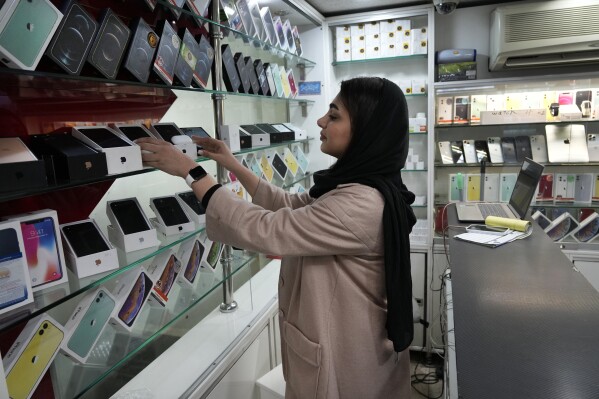 A cellphone vendor works at her shop in downtown Tehran, Iran, Wednesday, Feb. 21, 2024. Even though Supreme Leader Ayatollah Ali Khamenei has denounced American luxury goods amid years of tensions with the West, consumers still want the phones and the prestige associated with them. (AP Photo/Vahid Salemi)
