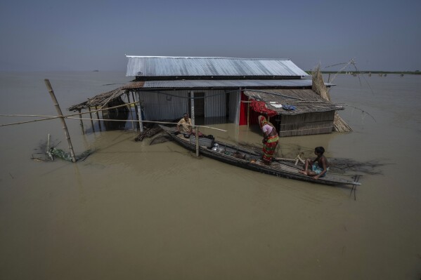 Yaad Ali, 55, left, and his wife Monuwara Begum, 45, center, and Musikur Alam, 14, leave their submerged house on a boat in the floodwaters in Sandahkhaiti, a floating island village in the Brahmaputra River in Morigaon district, Assam, India, Wednesday, Aug. 30, 2023. (AP Photo/Anupam Nath)