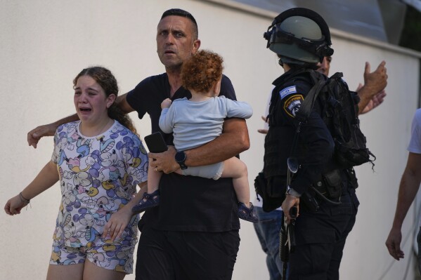 Israeli police officers evacuate a family from a site hit by a rocket fired from the Gaza Strip, in Ashkelon, southern Israel, Saturday, Oct. 7, 2023. (AP Photo/Tsafrir Abayov)