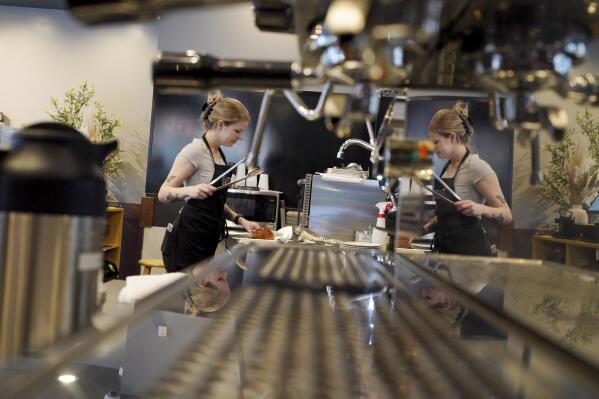 Reflected in the stainless steel of an espresso machine, store manager Kimberly Coblish, of Broomfield, Colo., handles a pastry for a customer at Tea with Tae on the 16th Street Mall in this photograph taken Wednesday, Sept. 14, 2022, in Denver. The store is part of Denver's Pop-Up Denver, a program to offer free rent to pop-up businesses that agree to do business downtown for a period of time. (Hart Van Denburg/Colorado Public Radio via AP)