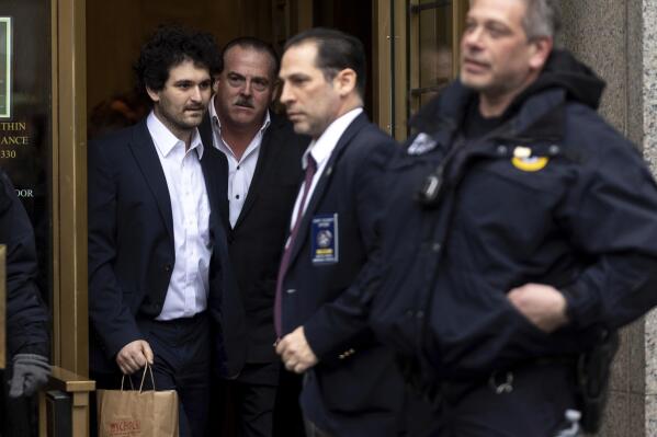 FTX founder Sam Bankman-Fried, left, is escorted to his car from the U.S. District Court in Manhattan, Thursday, Dec. 22, 2022, in New York. Bankman-Fried's parents agreed to sign a $250 million bond and keep him at their California home while he awaits trial on charges that he swindled investors and looted customer deposits on his FTX trading platform. (AP Photo/Julia Nikhinson)