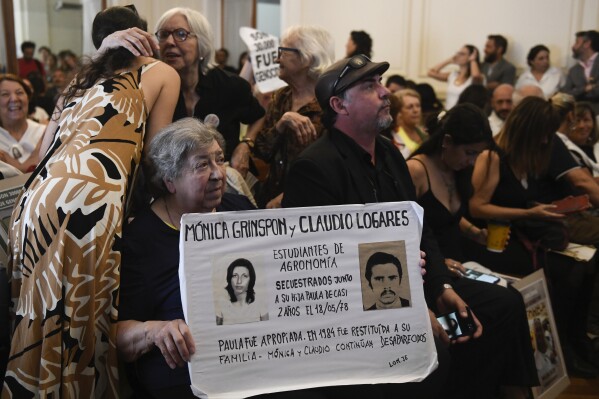 Personas sostienen fotografías de desaparecidos en un tribunal mientras escuchan el veredicto para expolicías y exmilitares procesados por crímenes de lesa humanidad durante la dictadura en La Plata, Argentina, el martes 26 de marzo de 2024. (AP Foto/Gustavo Garello)