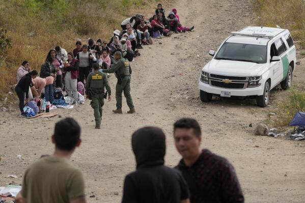 Agentes de la Patrulla Fronteriza hablan con mujeres migrantes antes de llevarlas a una vagoneta mientras esperan a solicitar asilo entre dos muros fronterizos, el jueves 11 de mayo de 2023, en San Diego. (AP Foto/Gregory Bull)