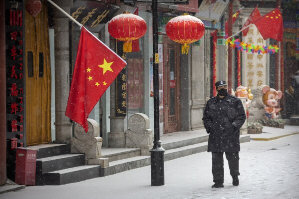 FILE - In this Feb. 5, 2020, file photo, a security guard wears a face mask as he walks along a pedestrian shopping street during a snowfall in Beijing. China’s ruling Communist Party faces a politically fraught decision: Admit the outbreak of a new virus isn’t under control and cancel this year’s highest-profile official event. Or bring 3,000 legislators to Beijing next month and risk fueling public anger at the government’s handling of the disease. (AP Photo/Mark Schiefelbein, File)