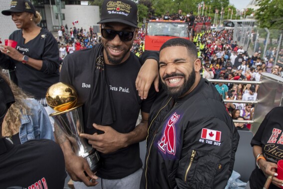FILE - Toronto Raptors' Kawhi Leonard, front left, holds his MVP trophy while posing with rapper/producer Drake as they celebrate during the team's NBA basketball championship parade in Toronto, June 17, 2019. Just as a movie soundtrack helps viewers follow the action of the narrative through each plot twist, hip-hop has done the same for basketball via the NBA. Drake has been a global ambassador for his hometown team the Toronto Raptors since 2013 and is often seen on the sidelines interacting with coaches and players. (Frank Gunn/The Canadian Press via AP, file)