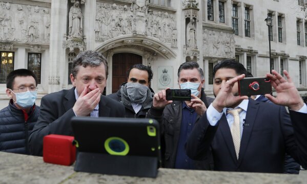 Uber drivers of the (ADCU), App Drivers & Couriers Union, listen to the court decision on a tablet computer outside the front of the Supreme Court in London, Friday, Feb. 19, 2021. The U.K. Supreme Court ruled Friday that Uber drivers should be classed as “workers” and not self employed.(AP Photo/Frank Augstein)