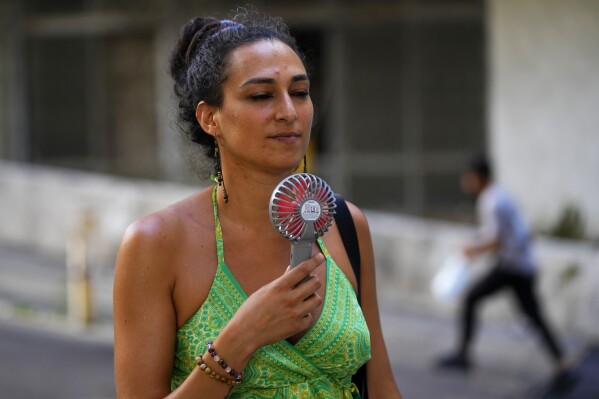 FILE - A woman cools off with an electric fan during on a sweltering hot day in Beirut, Lebanon, July 28, 2023. At about summer's halfway point, the record-breaking heat and weather extremes are both unprecedented and unsurprising, hellish yet boring in some ways, scientists say. (AP Photo/Hassan Ammar, File)