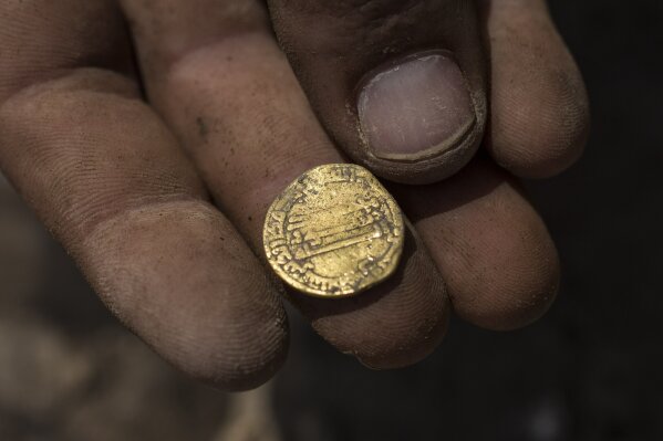 Israeli archaeologist Shahar Krispin displays a gold coin that was discovered at an archeological site in central Israel, Tuesday, Aug 18, 2020. Israeli archaeologists have announced the discovery of a trove of early Islamic gold coins during recent salvage excavations near the central city of Yavn Tel Aviv. The collection of 425 complete gold coins, most dating to the Abbasid period around 1,100 years ago, is a "extremely rare" find. (AP Photo/Sipa Press, Heidi Levine, Pool)