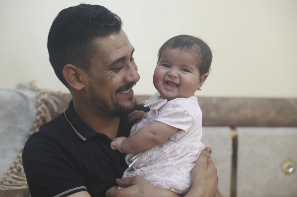 Khalil al-Sawadi plays with his adopted daughter Afraa in Jinderis, Syria, on Saturday, Aug. 5, 2023. Afraa was born under the rubble of her family home, destroyed by the deadly earthquake that hit Turkey and Syria six months ago, killing her parents and siblings. (AP Photo/Ghaith Alsayed)