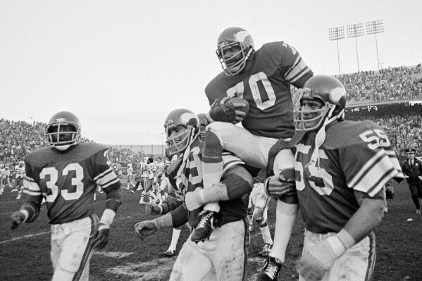 Minnesota Viking tackle Jim Marshall clutches the game ball as he is carried from the field by teammates Doug Southerland, left, and Scott Studwell after the Vikings defeated the Buffalo Bills 10-3 in an NFL football game in Bloomington, Minn., on Sunday, Dec. 9, 1979. (AP Photo/Jim Mone, File)