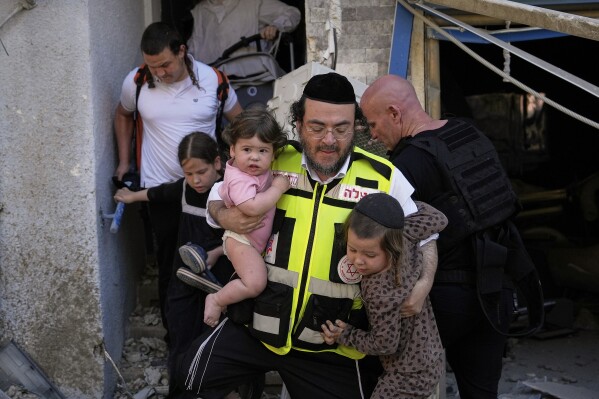 A rescue worker carries two children as residents evacuate from the site where a missile launched from Iran struck Haifa, Israel, Sunday, June 22, 2025. (AP Photo/Baz Ratner)