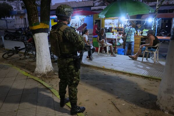 Residents gather under the watch of a soldier in Tibu, Colombia, on Monday, Jan. 20, 2025, following a series of guerrilla attacks that have killed dozens and forced thousands to flee their homes in the Catatumbo region. (AP Photo/Fernando Vergara)
