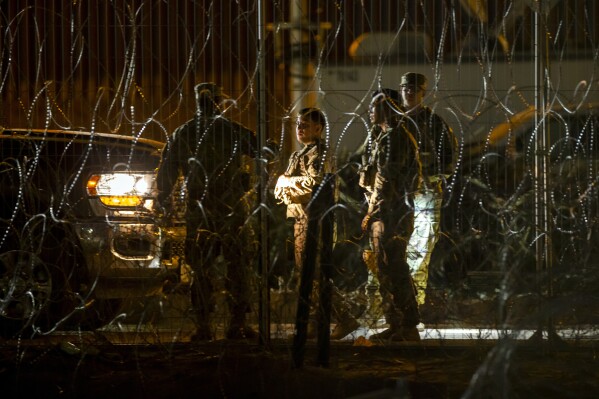 Texas Army National Guard members talk while patrolling behind razor wire on the banks of the Rio Grande in El Paso, Texas, seen from Ciudad Juarez, Mexico, late Thursday, Aug. 8, 2024. (AP Photo/Andres Leighton)