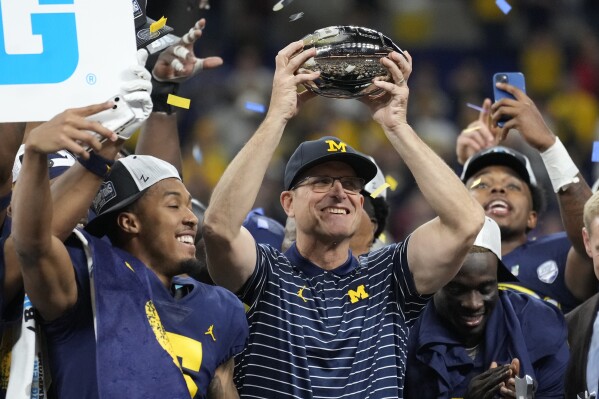FILE - Michigan head coach Jim Harbaugh holds the trophy as he celebrates with his team after defeating Purdue in the Big Ten championship NCAA college football game, early Sunday, Dec. 4, 2022, in Indianapolis. There could be some awkward trophy ceremonies around college football's championship weekend. (AP Photo/AJ Mast, File)