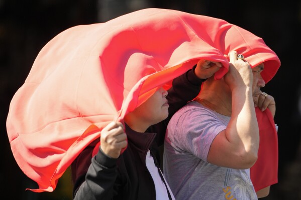 FILE - A man and a woman use a cloth over their heads to protect themselves from the sun in Manila, Philippines on April 29, 2024. In a world that has become increasingly accustomed to extreme weather extremes, the past few days and weeks seem to have taken those environmental impacts to extremes to a new level.  (AP Photo/Aaron Favela, File)