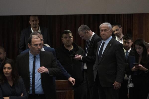 Israeli Prime Minister Benjamin Netanyahu, right, stands on the floor of the Knesset, the country's parliament, during a vote as people mass outside to protest his government's plan to overhaul the judicial system, in Jerusalem, Monday, March 27, 2023. (AP Photo/ Maya Alleruzzo)