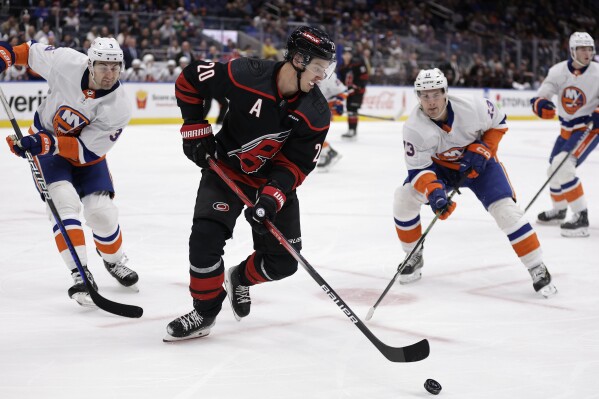 Carolina Hurricanes center Sebastian Aho (20) controls the puck in front of New York Islanders center Mathew Barzal (13) and defenseman Adam Pelech (3) during the first period of an NHL hockey game Tuesday, March 19, 2024, in Elmont, N.Y. (AP Photo/Adam Hunger)