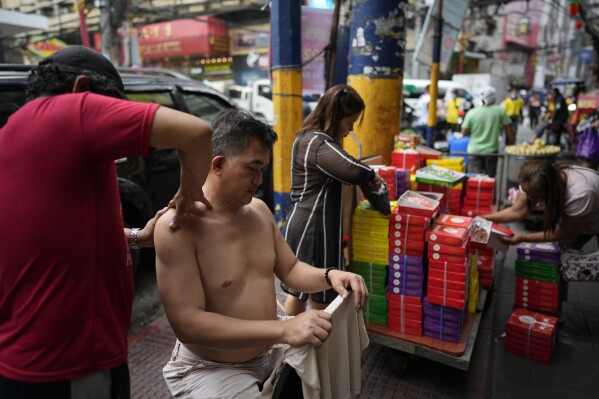 A man massages a costumer along a street at Binondo district, said to be the oldest Chinatown in the world, in Manila, Philippines on Monday, Feb. 5, 2024. Crowds are flocking to Manila's Chinatown to usher in the Year of the Wood Dragon and experience lively traditional dances on lantern-lit streets with food, lucky charms and prayers for good fortune. (APPhoto/Aaron Favila)