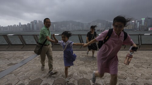 Mainland Chinese tourists run along a promenade during a typhoon in Hong Kong, Monday, July 17, 2023. Schools and the stock market were closed in Hong Kong on Monday as Typhoon Talim swept south of the city. (AP Photo/Louise Delmotte)