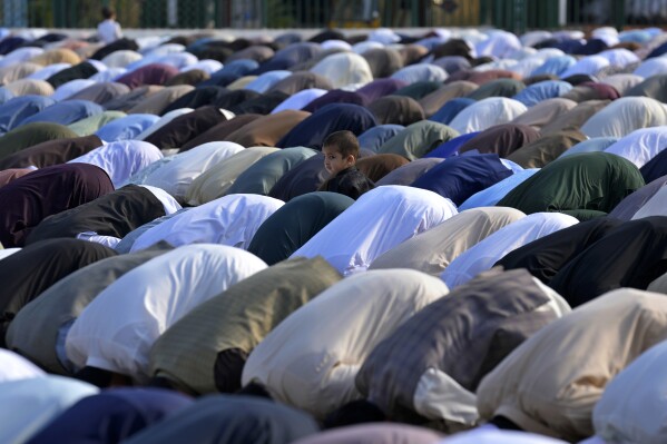 A Muslim child stands beside his father performing an Eid al-Fitr prayer with others, marking the end of the fasting month of Ramadan, in Rawalpindi, Pakistan, Wednesday, April, 10, 2024. (AP Photo/Anjum Naveed)