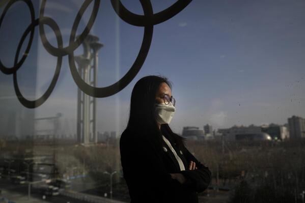 Olympic Games worker Cathy Chen stands for a photo in the main media center at the 2022 Winter Olympics, Friday, Feb. 11, 2022, in Beijing. In her mind, Chen pictures a scene that she herself says could be drawn from a TV drama: Falling into the arms of her husband after long months apart, when he meets her off the plane from Beijing. Scooping up their two young daughters and squeezing them tight. "I just imagine when we’re back together,” the Olympic Games worker says, "and I just can’t control myself.” (AP Photo/Jae C. Hong)
