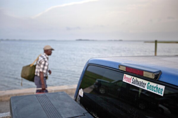 FILE - A sticker celebrating the Geechee heritage is seen on a pickup truck, June 10, 2013, as passengers board a ferry to the mainland from Sapelo Island, Ga. One of the few remaining Gullah-Geechee communities in the U.S. is in another fight to hold onto land owned by residents' families since their ancestors were freed from slavery. The few dozen remaining residents of the tiny Hogg Hummock community on Georgia's Sapelo Island were stunned when they learned county officials may end zoning protections enacted nearly 30 years ago to protect the enclave from wealthy buyers and tax increases. (AP Photo/David Goldman, File)