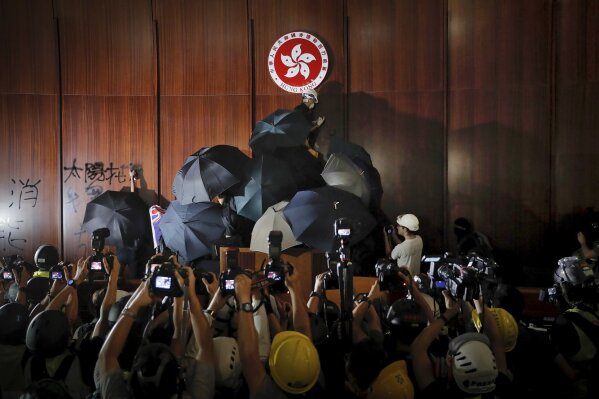 FILE - In this July 1, 2019, file photo, journalists photograph a protester defacing the Hong Kong emblem inside the meeting hall of the Legislative Council in Hong Kong. From across the political spectrum, Hong Kong residents condemned mob violence at the U.S. Capitol, 18 months after they saw protesters storm their own local legislature. (AP Photo/Kin Cheung, File)