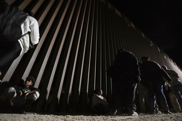 People line up against a border wall as they wait to apply for asylum after crossing the border from Mexico Tuesday, July 11, 2023, near Yuma, Arizona. (AP Photo/Gregory Bull)