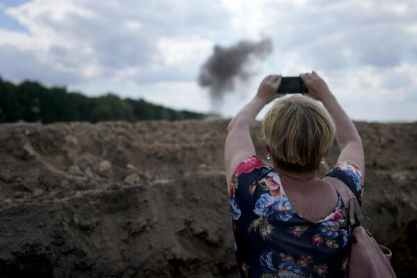 A journalist takes a picture of smoke rising from a landmine exploded by a Ukrainian specialized team working on a field to clean the area on the outskirts of Kyiv, Ukraine, Thursday, June 9, 2022. (AP Photo/Natacha Pisarenko)
